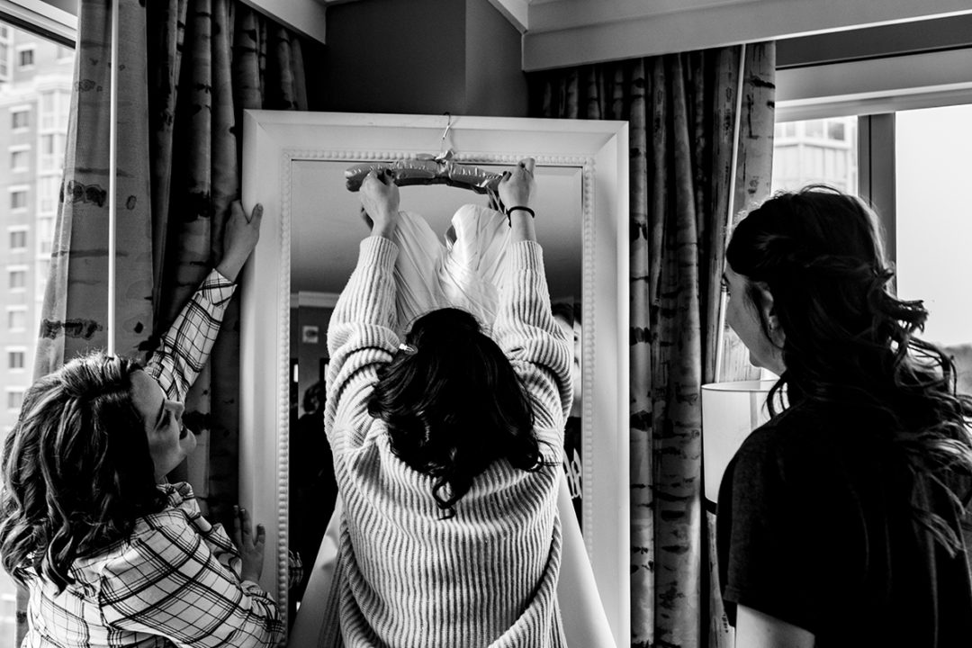 Hanging up the bridal dress by bridesmaids against a mirror at the Westin in Old Town Alexandria by DC wedding photographers Potok's World Photography