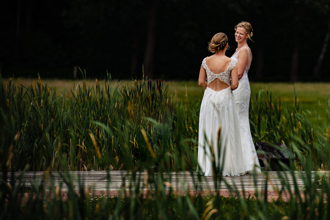 First Look Wedding Pros and Cons. Outdoor first look on bridge by two brides in wedding dresses by DC wedding photographers Potok's World Photography