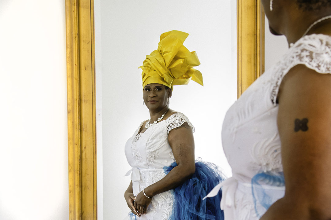  Ghanaian bride getting ready wearing traditional headdress and looking in the mirror at Fathom Gallery during her Washington DC micro wedding by Potok's World Photography