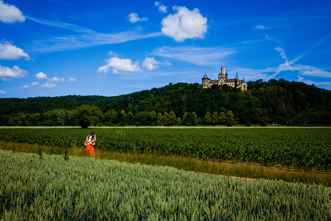 Drone shot of Couple in the fields outside with the castle in the background during Marienburg Castle engagement photos in Germany by Washington DC wedding photographers Potok's World Photography