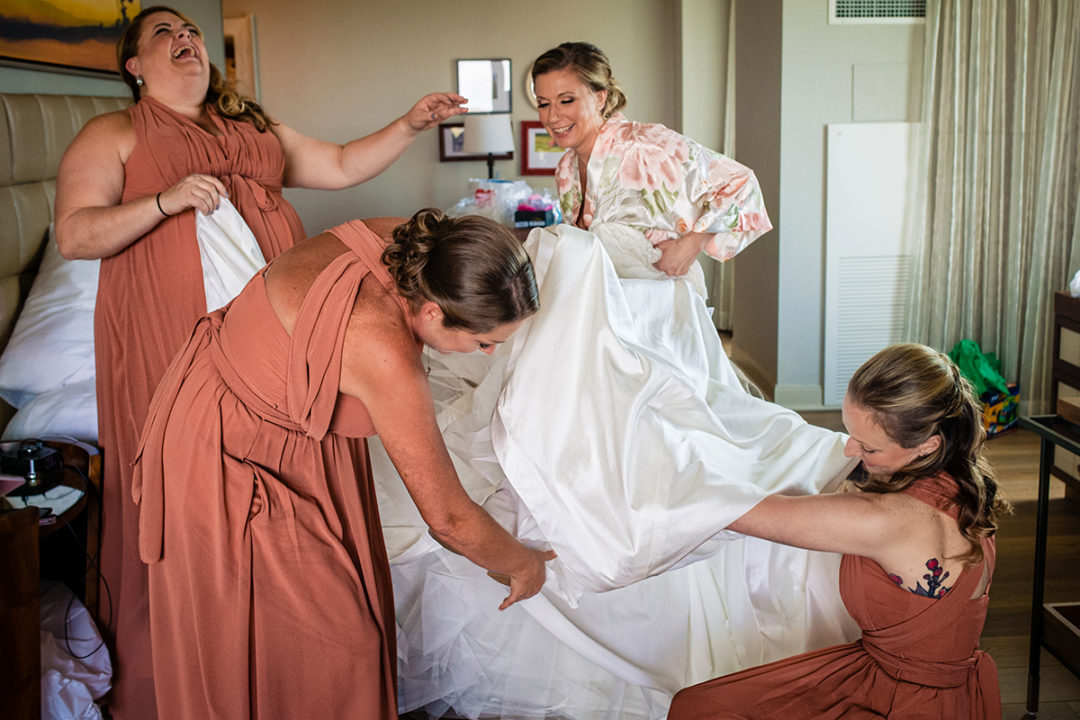 Bride getting into bridal dress with her bridesmaids at Lansdowne Resort and Spa in Leesburg before her Vanish Brewery wedding by DC wedding photographers Potok's World Photography